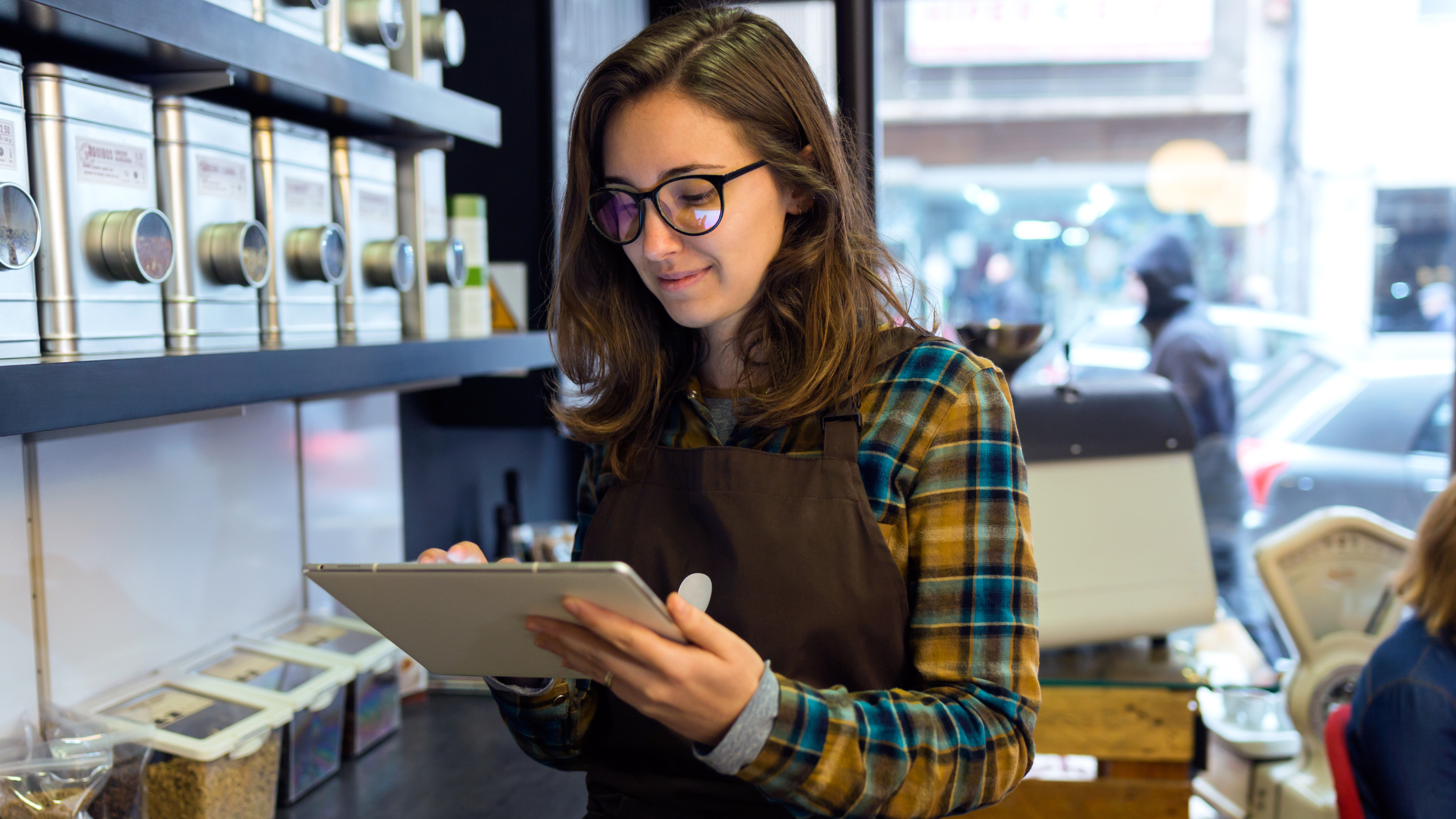A young woman with short dark hair and glasses reading from a tablet in a store